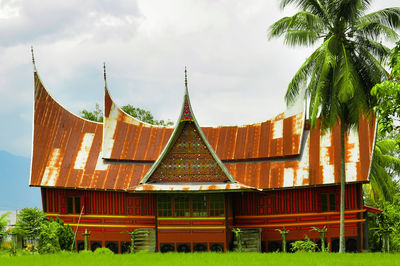 Traditional building by trees on field against sky