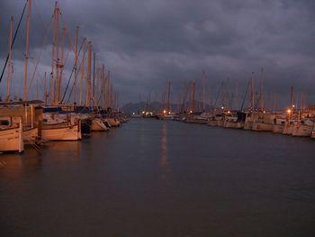 Sailboats moored at harbor against sky at dusk
