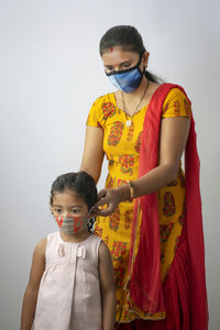 Mother and daughter wearing flu mask standing against white background