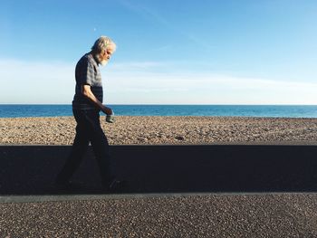 Side view of man walking on beach against sky