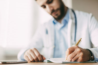 Friendly young male doctor of oriental appearance sits at a desk in his office and takes notes 