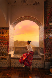 Rear view of woman with arms outstretched at sunset