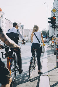 Rear view of business colleagues standing with bicycle at signal in city