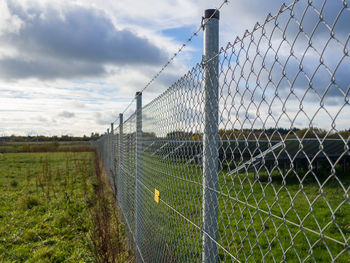 Metal fence at solar energy farm on field against sky, germany