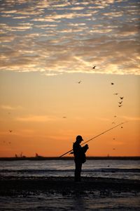 Silhouette man fishing in sea against sky during sunset