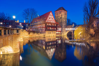 Arch bridge over river by buildings against sky at dusk