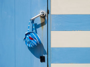 Blue and white striped child's hat hanging on the door handle of a blue and white striped beach hut