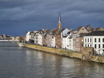 Buildings by river against sky