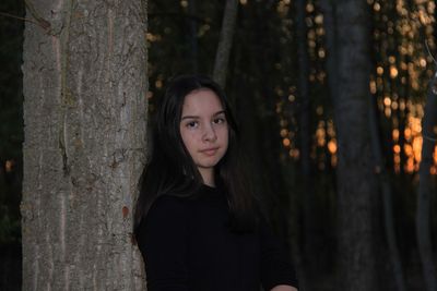 Portrait of beautiful young woman against tree trunk in forest