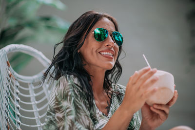 Portrait of a smiling young woman holding sunglasses