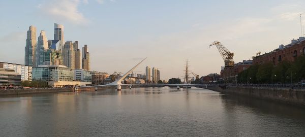 Bridge over river by buildings against sky in city