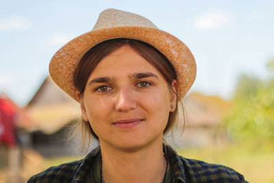 Close-up light smiling young brunette caucasian woman in hat. summer blurred village nature bokeh 