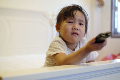 Portrait of girl watching tv while sitting on bed at home