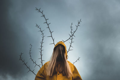 A girl with long hair in a yellow hood, with the back of a tree with thorns. concept of depression