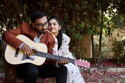 Young couple sitting on guitar against plants