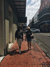 Full length of friends walking on sidewalk in city
