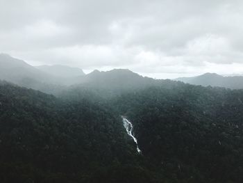 Scenic view of waterfall and mountains against cloudy sky