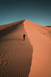 Rear view of man walking on sand in desert against clear sky