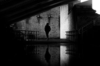 Rear view of silhouette man standing by railing in canal amidst bridge