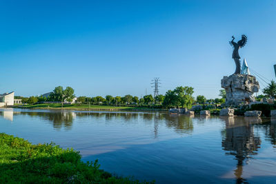 Statue in lake against clear blue sky