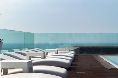 Empty chairs by swimming pool against sky