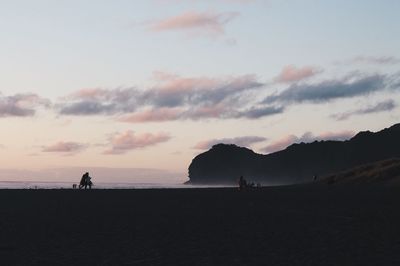 Silhouette people standing on beach against sky during sunset