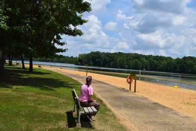 Woman sitting on bench by street against cloudy sky at holy ground battlefield park