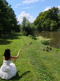 Rear view of woman sitting by lake against sky