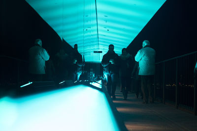Rear view of people walking on illuminated corridor