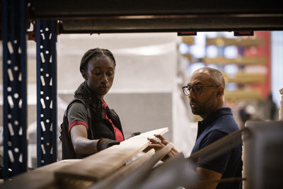 Saleswoman with male customer removing plank from rack at hardware store