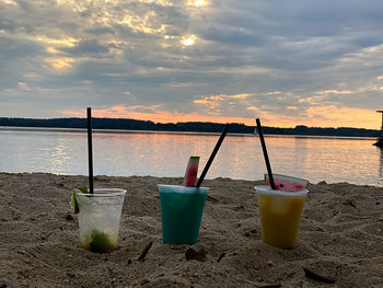 Lounge chairs and tables at beach against sky during sunset