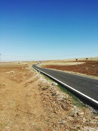 Empty road by landscape against clear blue sky