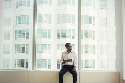 Businessman sitting on window sill holding digital tablet