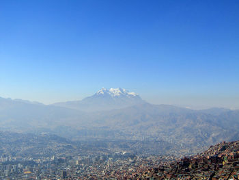Aerial view of city by mountains against clear blue sky