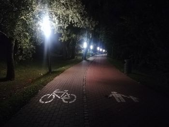 Illuminated street amidst trees at night