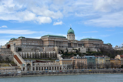 Danube river by buildings and buda castle against cloudy sky