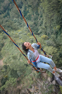 High angle view of cheerful woman swinging over trees 