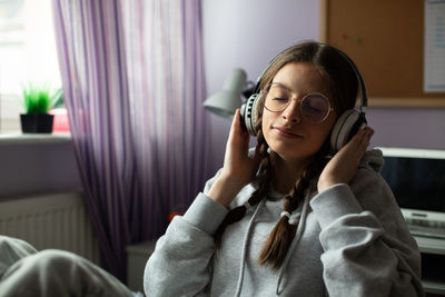 A teenage girl listens to music on wireless headphones with her eyes closed.