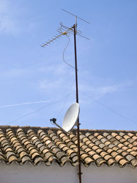 Low angle view of telephone pole on roof of building against sky