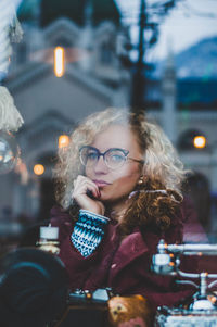 Thoughtful young woman looking away while sitting in cafe seen through glass window