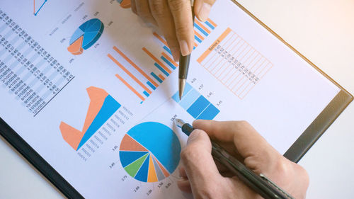 Cropped image of business people discussing over graphs at desk