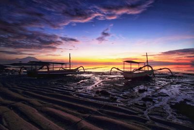 Boat moored on beach against sky during sunset