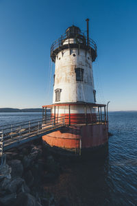 Lighthouse by sea against clear sky