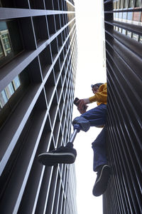 Young man with leg prosthesis using smart phone while sitting on railing against skyscraper