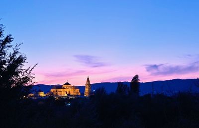 Silhouette buildings by trees against sky during sunset