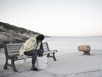 Rear view of man on seat at beach against clear sky