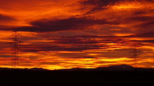 Silhouette electricity pylon against dramatic sky during sunset