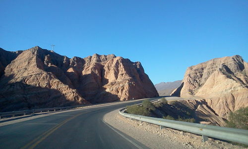 Road leading towards mountains against blue sky