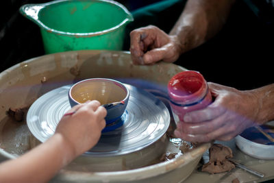 Hands with a brush and paints and a ceramic plate on a potter's wheel