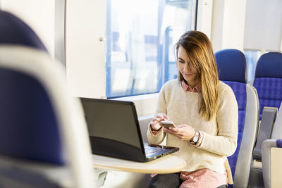 Businesswoman using smart phone while traveling in train